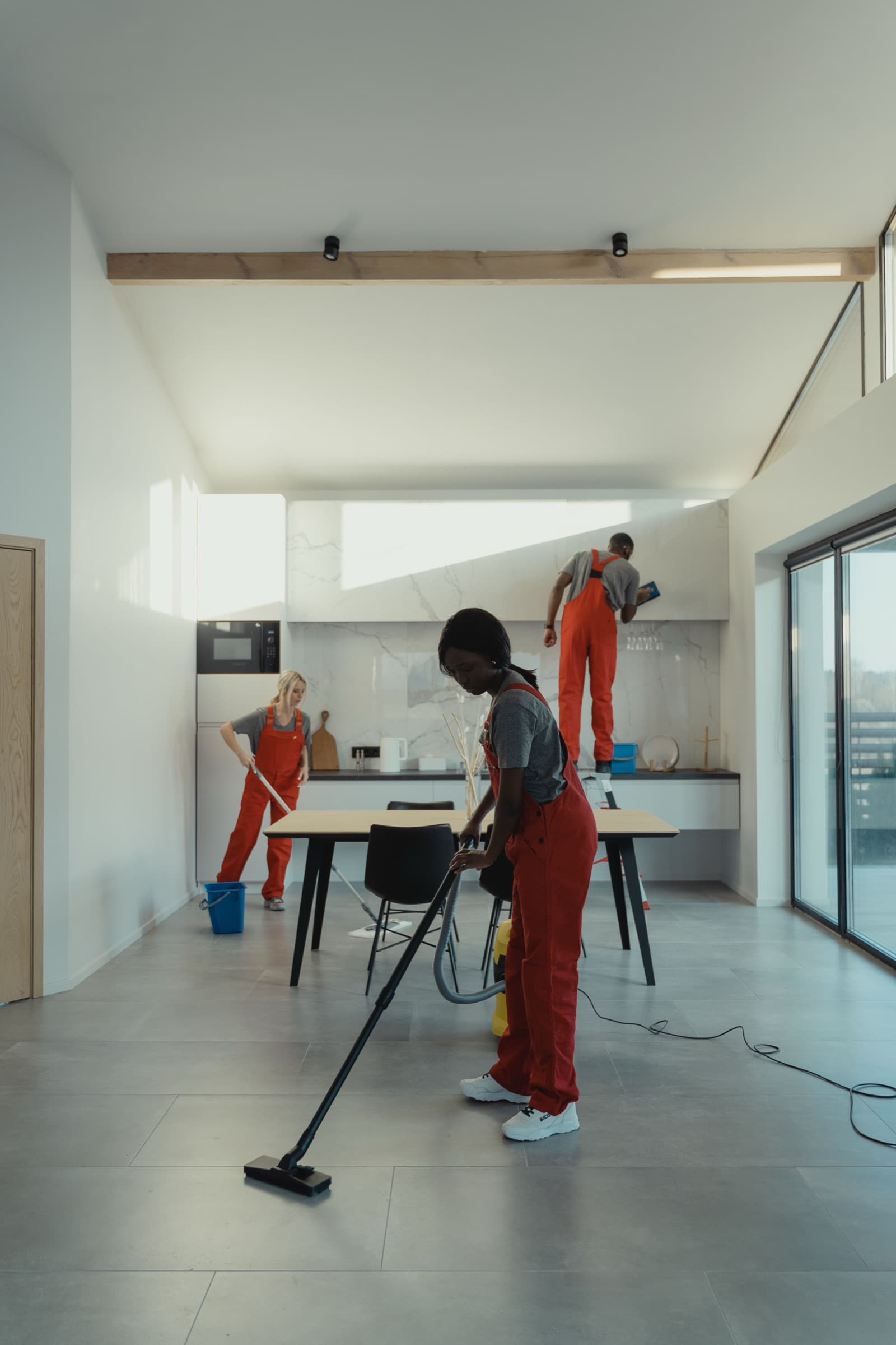 Three cleaners vacuuming and wiping surfaces in a bright open-plan room