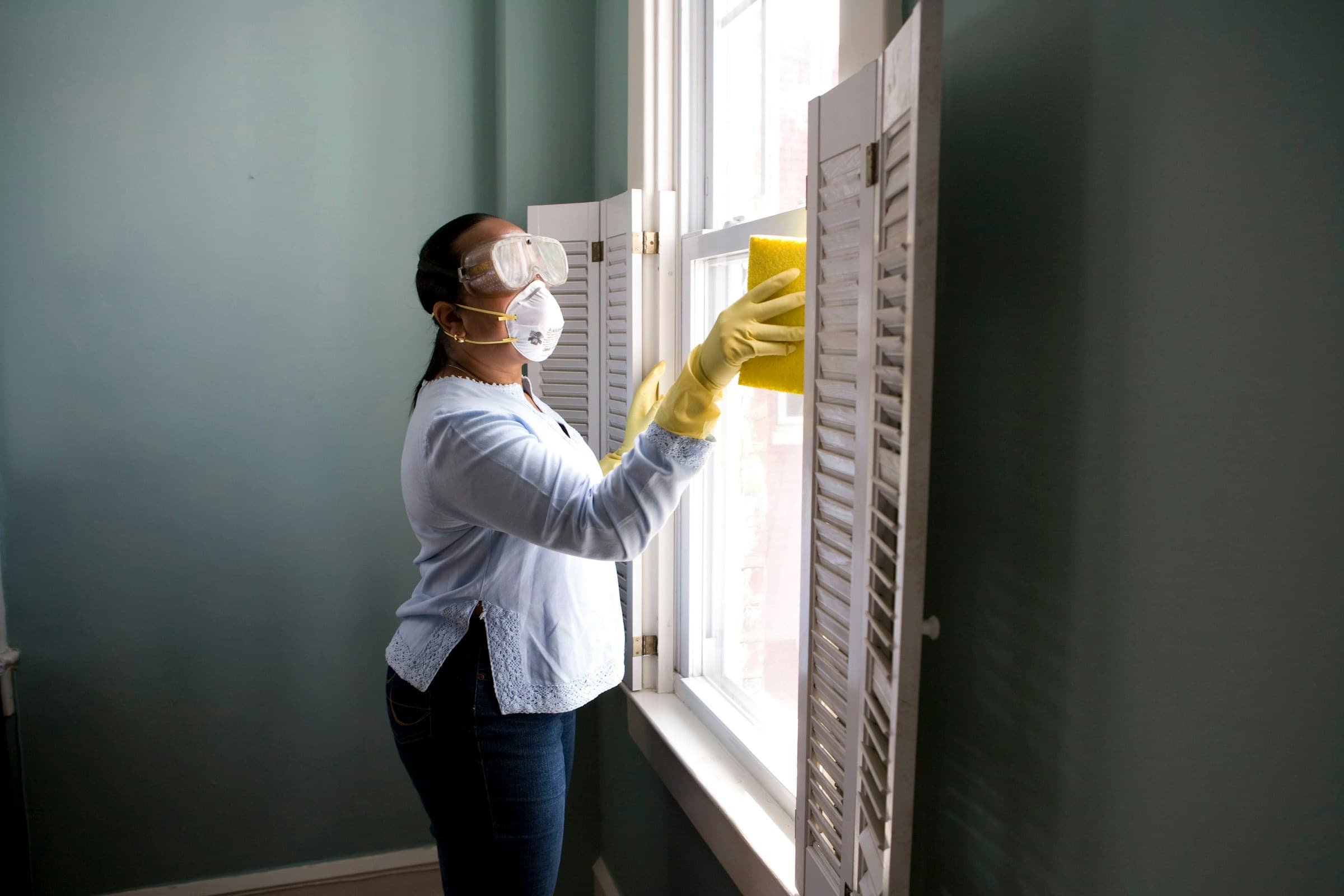 Cleaner in yellow gloves wiping a window in a bright room