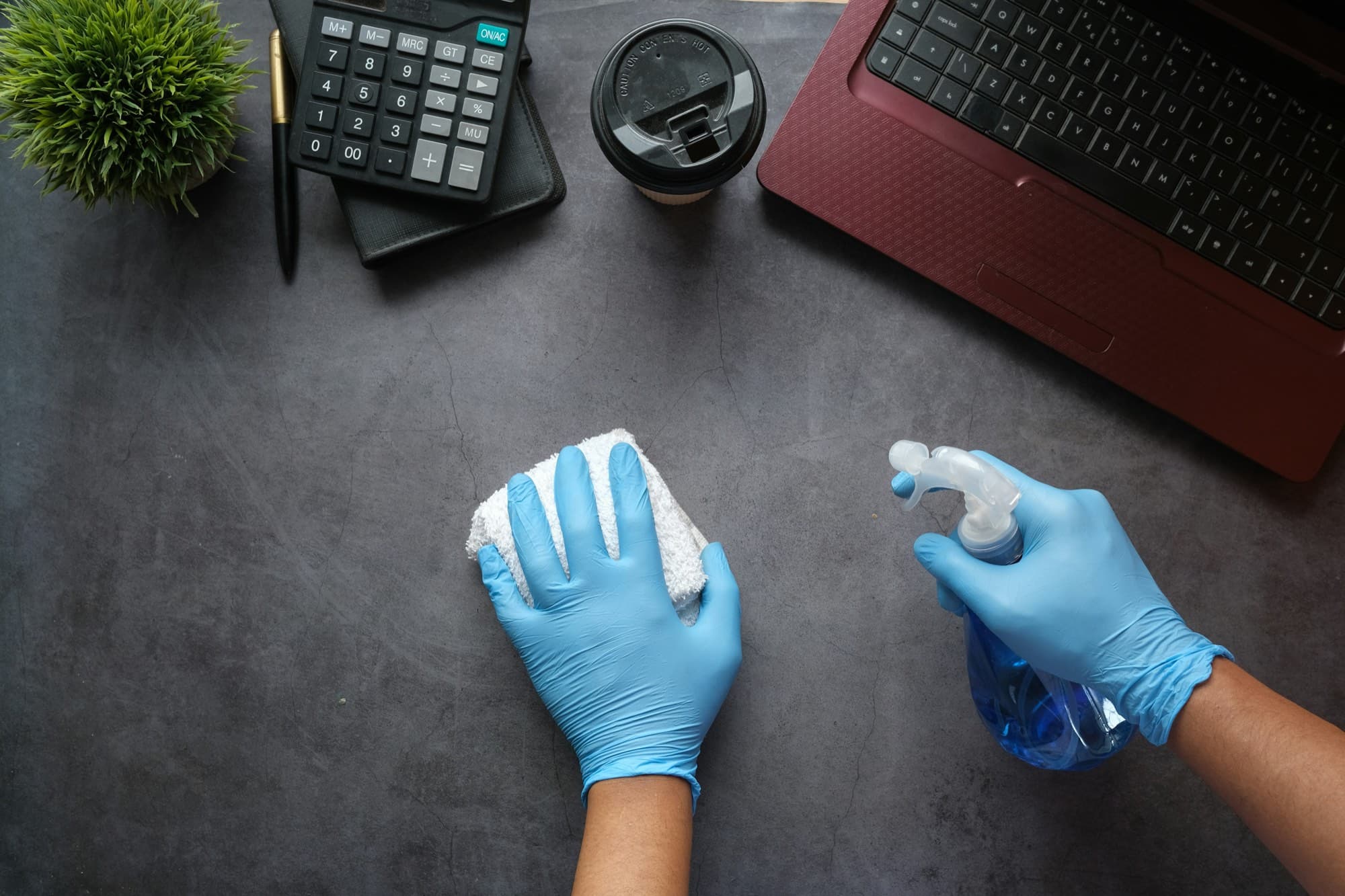 Gloved hands wiping an office desk next to a laptop